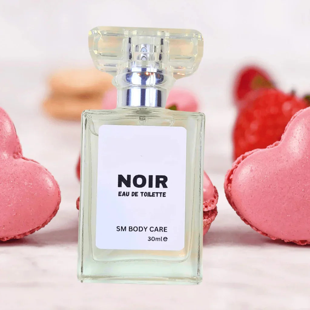 Perfume bottle labeled 'NOIR' with heart-shaped macarons and strawberries in the background
