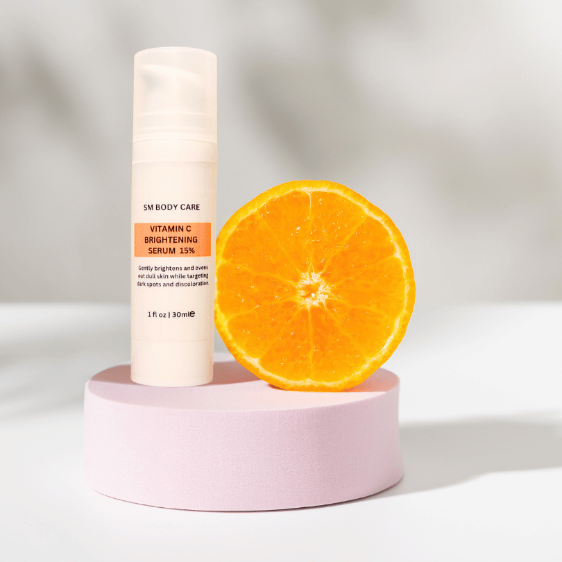 A bottle of Vitamin C Brightening Serum 15% is displayed next to a sliced orange, presented on a pink pedestal with a bright background.